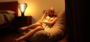 Australian girl sitting in grey bean bag sofa gaming chair with yellow lighting beside bed