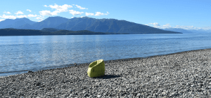 Outdoor green bean bag sofa chair sits on gravel facing the lake under the heat of the sun