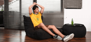 Australian man in yellow thrilled for Olympics in black sapphire Acoustic bean bag Sofa with beer bottle on top of the the black wing ottoman