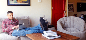 Man in chekered shirt typing on his laptop while sitting on grey bean bag sofa chair