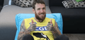 Tattooed man wearing yellow jersey shirt sits in blue bean bag chair with two thumbs up